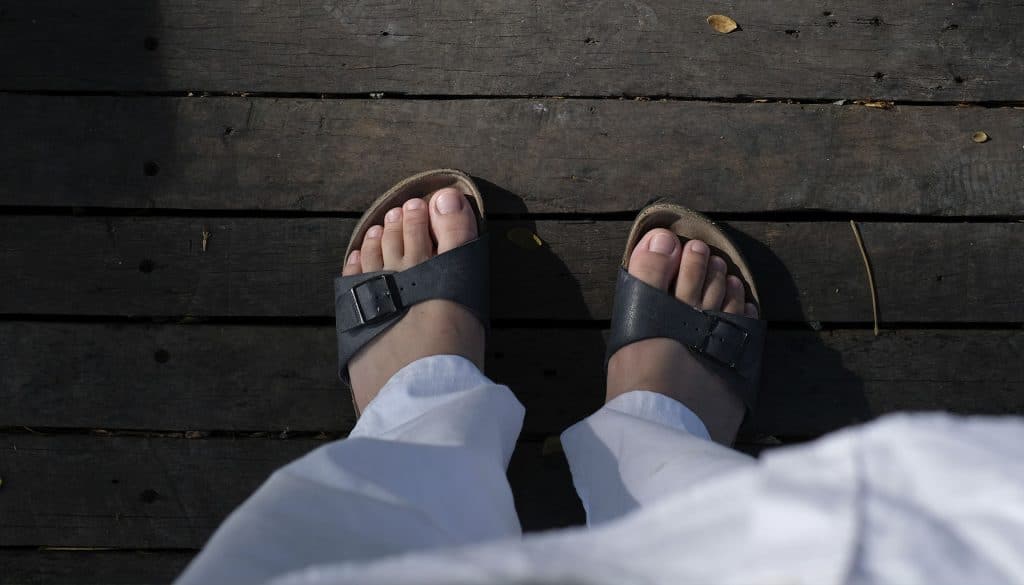 Piedi con ciabatte con plantare anatomico su pavimento in legno, simbolo di comfort e stile quotidiano